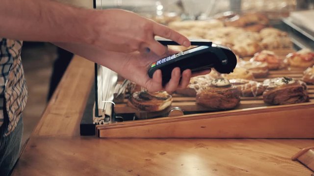 Close-up of woman making payment through NFC in bakery, cafe restaurant, mobile phone contactless pay for bill with terminal, banking