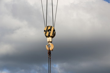 Obraz premium Hook big gantry crane made of metal colored yellow against a background of bright blue sky with clouds close-up