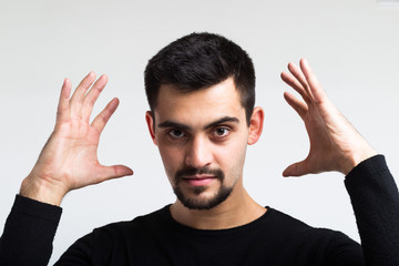 A young man with a force tries to squeeze the air around his head. Widely spaced fingers, wide palms, strong eyes. Portrait.