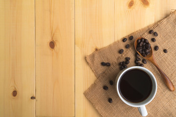 A cup of coffee and coffee bean grain on sack fabric put on pine wood table background include copyspace for add text or graphic