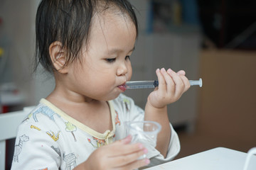 Baby asian toddler girl feeding medicine by themself