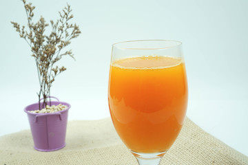 Fresh orange juice or carrot juice in wine cup with dry flower background in purple pot isolated on white