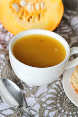 Pumpkin soup in white mug on table.