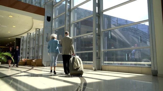 Two senior people walking together with a suitcase in airport terminal
