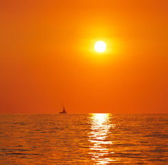 Sunset or sunrise over the sea. On the horizon a yacht.