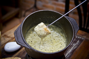 High-angle close-up of rustic fondue in a classic cast-iron pot, creamy cheese with garlic and herbs, bread dipped with metal fork for perfect melted texture.