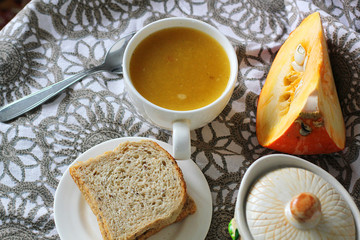 Pumpkin soup in white mug on table.