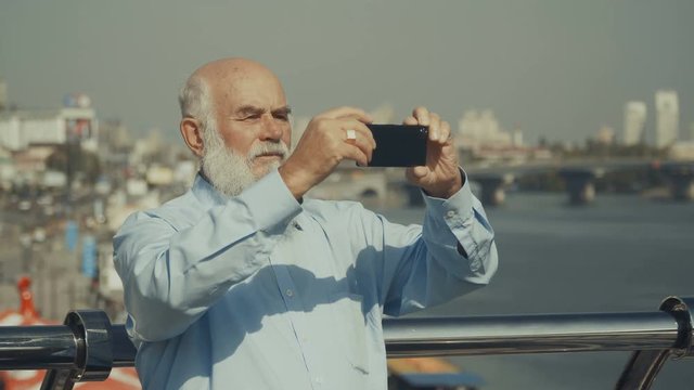 Pleasant elderly man takes a photo of the river