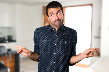 Brunette man pointing to the laterals having doubts inside house