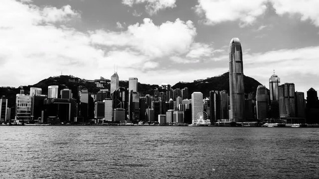 Hong Kong. Skyline of Hong Kong during the day. Beautiful skyscrapers with colorful cloudy sky. Time-lapse with boats. Black and white