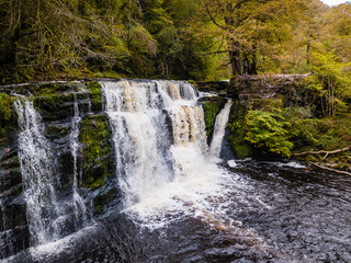 A picturesque waterfall (Sgwd Y Pannwr) in a tree lined river valley during the autumn