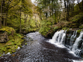 A picturesque waterfall (Sgwd Y Pannwr) in a tree lined river valley during the autumn