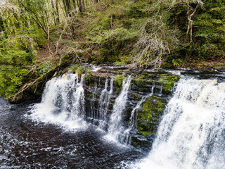 A picturesque waterfall (Sgwd Y Pannwr) in a tree lined river valley during the autumn