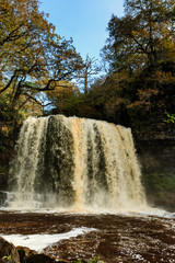 A large waterfall (Sgwd Yr Eira) in a tree lined gorge