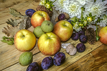 Prunes,apples,figs and green nuts with a bouquet of white dahlias on wooden boards