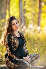 portrait of a beautiful pregnant young girl against a background of autumn forest. In fashionable clothes. Photo concept of pregnant women