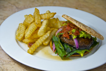 High-angle view of a healthy burger with grilled portobello, creamy guacamole, and crispy French...