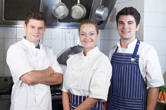 Portrait Of Chef And Staff Standing By Cooker In Kitchen