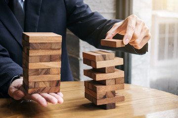Alternative risk concept, plan and strategy in business, Young intelligent businessman playing the wood game, hands of executive cooperate placing wood block on the tower, Collaborative management