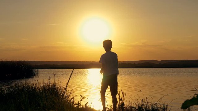 Silhouette of a boy throwing stones in the water against the background of an orange sunset