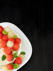 White cake decorated with watermelon, melon and kiwi ball-shaped pieces on a dark background. Copy space