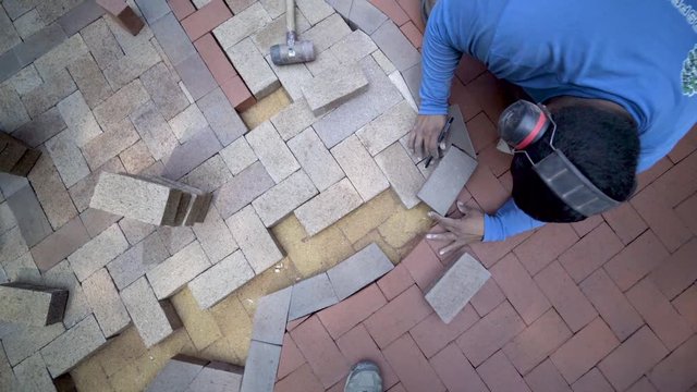 Hardscaping sculptor wearing ear protection fitting specially cut brick paver into place for marking the cuts, then set it aside and marks brick.