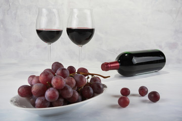 Two glasses of red wine with bottle and grapes