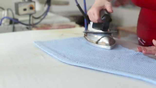Female worker work with professional ironing appliance at textile factory.