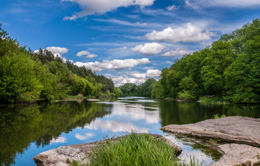 Summer landscape of the river, blue sky with clouds, reflections in the water, woods and stones. The river Ros, Ukraine.