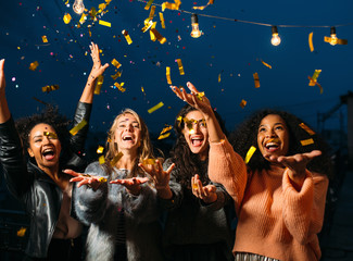 Happy women throwing confetti in the air. Friends celebrating outdoors.