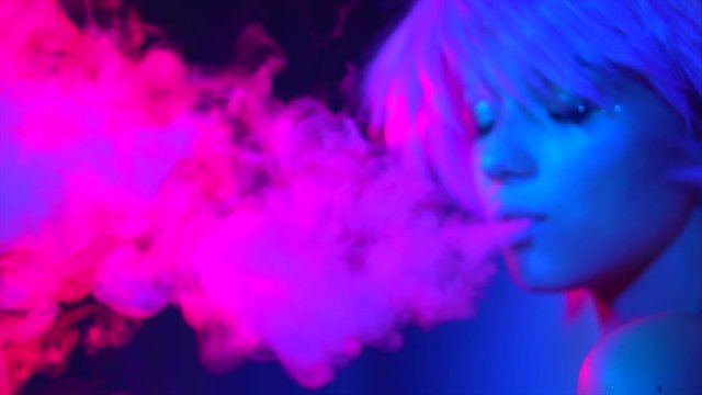 Beauty smoking girl in bright lights with colorful smoke. Woman inhaling from an electronic cigarette. Slow motion 4K UHD video 3840x2160