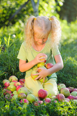 Little cute girl with blond hair  collects the apples scattered on a grass vertical photo, blurred background