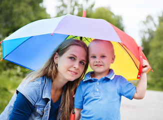 Portrait of a mother with her son under a rainbow umbrella on a nature background