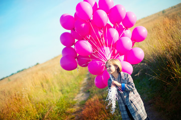 Happy toddler birthday girl in autumn field holding many pink balloons,smiling and laughing ready...
