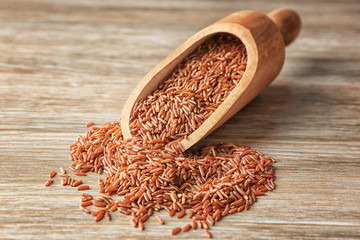 Scoop and heap of red Cargo rice on wooden background