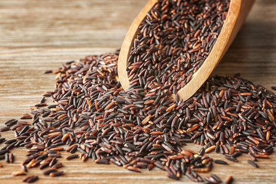 Scoop and heap of wild rice on wooden background