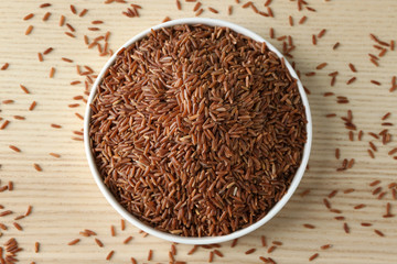 Bowl with raw red Cargo rice on wooden background
