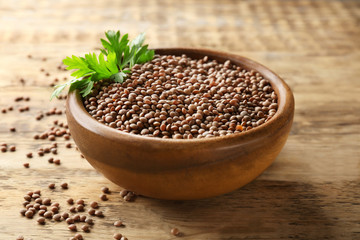 Bowl with brown lentils on wooden background