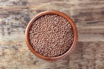 Bowl with brown lentils on wooden background