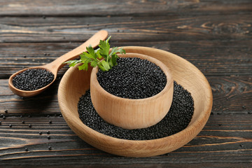 Composition with black lentils in kitchenware on wooden background