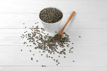 Ceramic bowl and spoon with french green lentils on wooden background