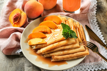 Plate with tasty thin pancakes and peaches on table