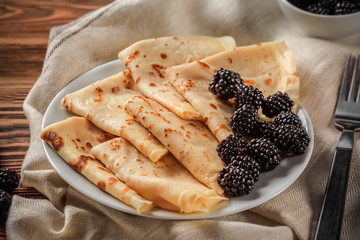 Plate with delicious thin pancakes and blackberries on table