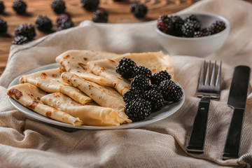 Plate with delicious thin pancakes and blackberries on table