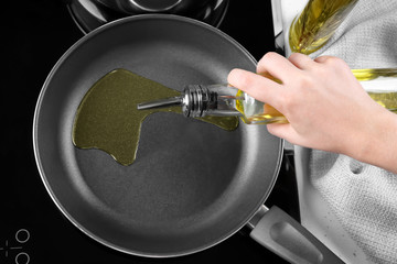 Woman pouring oil from bottle into frying pan in kitchen