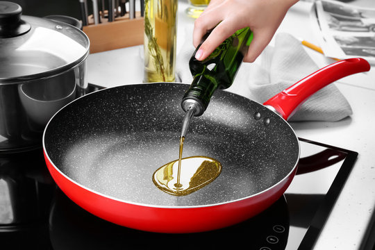 Woman pouring oil from bottle into frying pan in kitchen