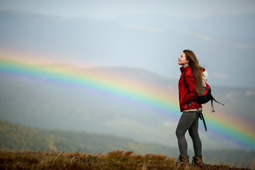 Mountain landscape with a rainbow. Girl tourist in mountain. Shot of a young woman looking at the landscape while hiking in the mountains. Travel inspiration and motivation, beautiful landscape