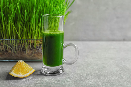 Wheat grass shot and slice of lemon on grey background