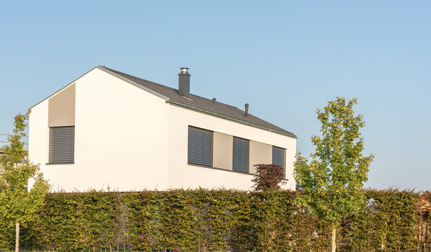 Modernes Haus mit Außenjalousien mit hoher Hecke als Sichtschutz