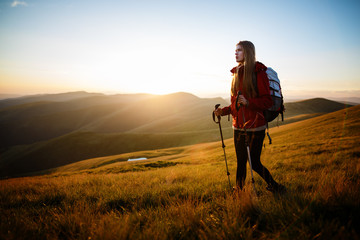 Shot of a young woman looking at the landscape while hiking in the mountains. Happy traveler with backpack standing on top of a mountain and enjoying sunset view